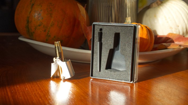 A Golden Birdie. The background has an autumnal centerpiece behind it, various gourds can be seen behind the Golden Birdie. The case is open, exposing the foam cutout, next to the birdie, standing tall.